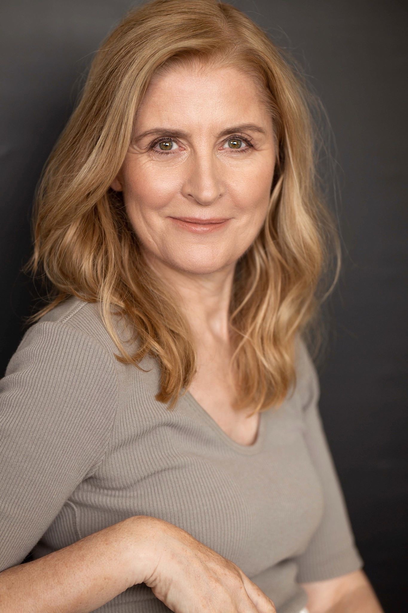 Headshot of Award-nominated Casting director Jo Briant from Fountainhead Casting wearing a beige shirt, sitting on a chair, smiling at the camera.